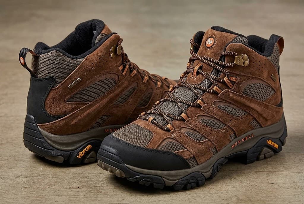 A pair of brown Merrell mid-height hiking boots with black toe caps and visible Vibram markings.