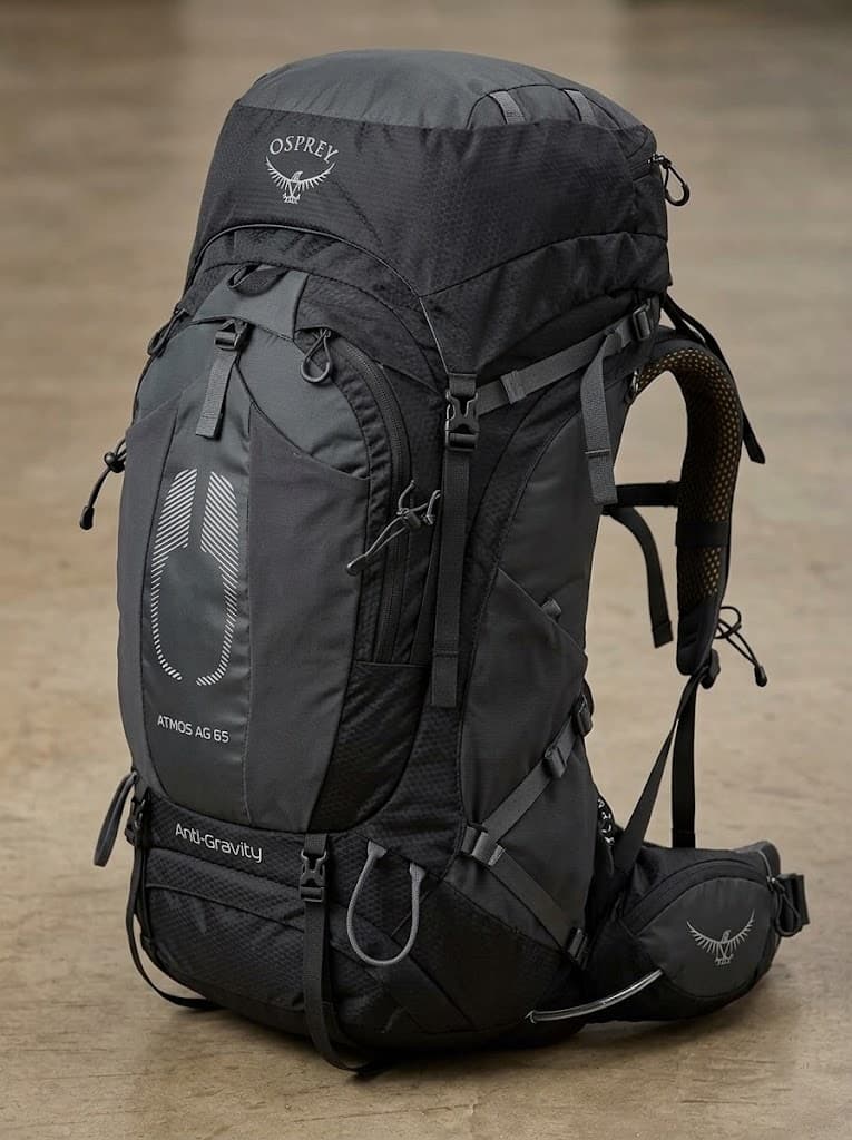 A black Osprey backpack marked Atmos AG 65, with a top lid, front pocket and padded hip belt.
